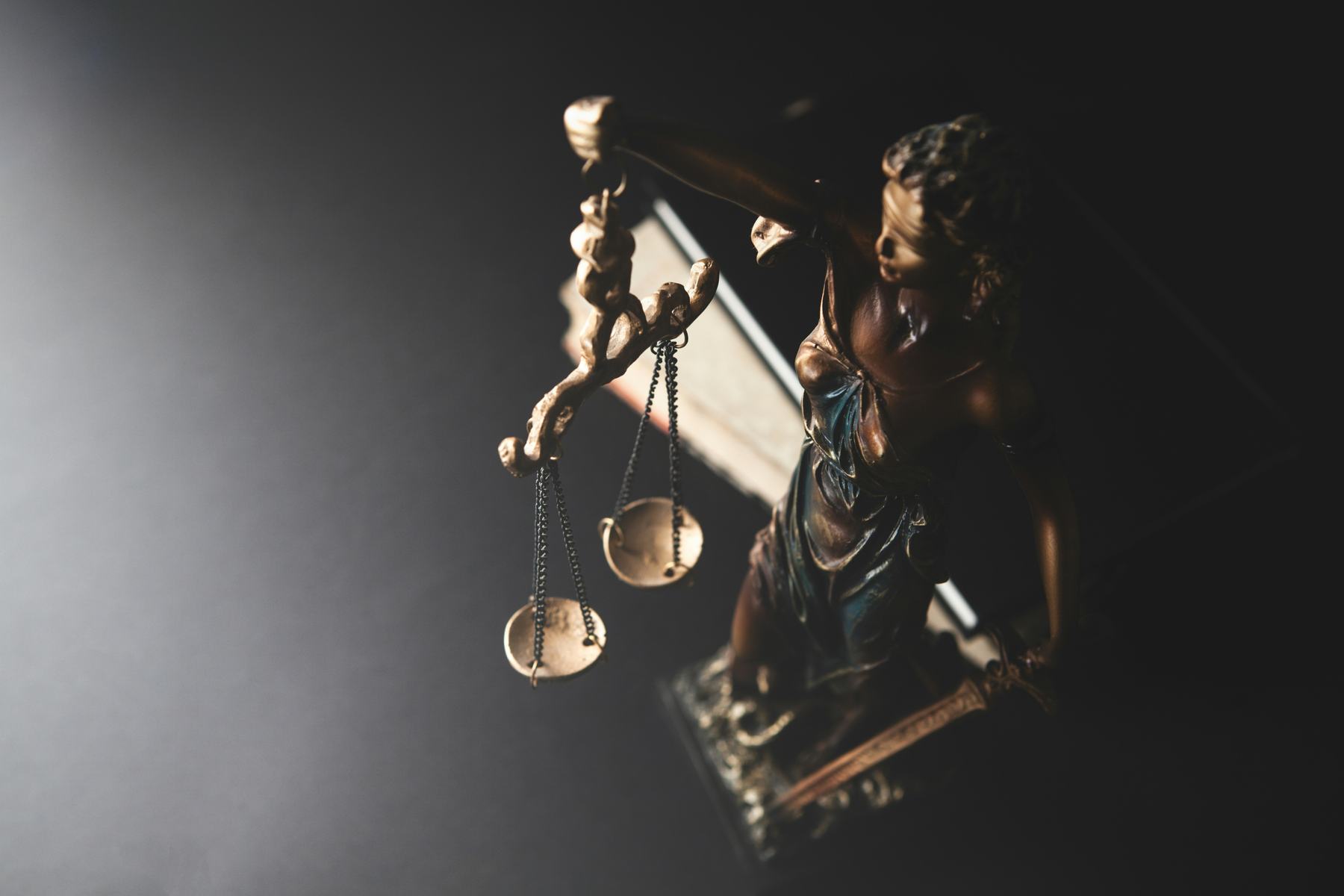 Estátua da Justiça com a balança, sob luz dura e fundo escuro