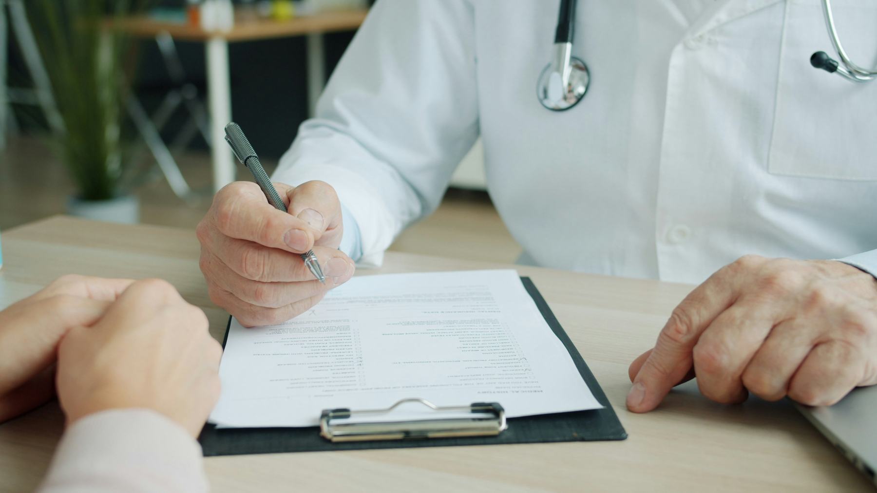 Médico preenchendo uma ficha de anamnese em consulta com paciente